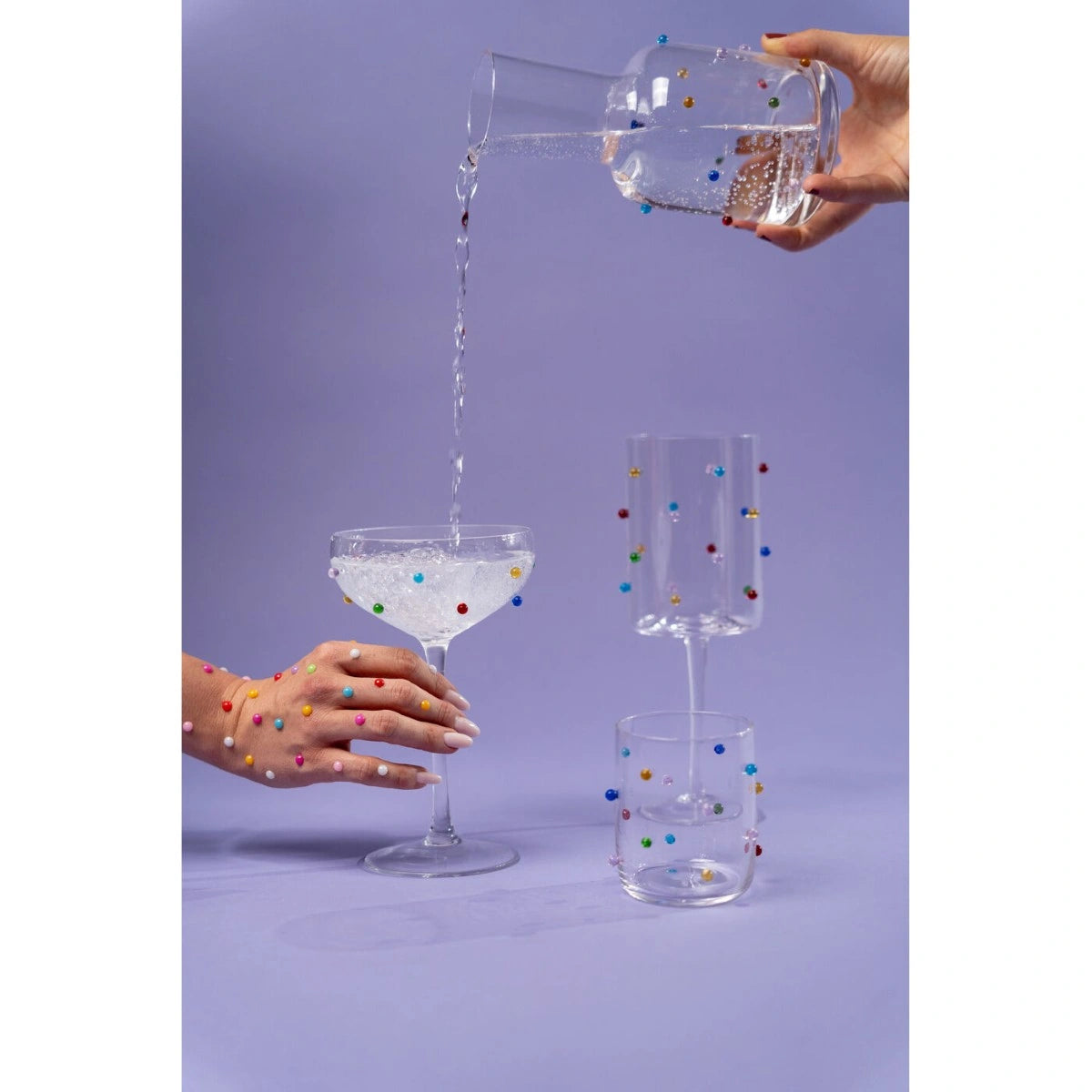 Hand pouring a colorful drink into a glass with a purple background