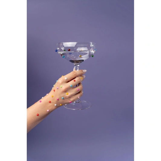 Hand holding a clear glass with colorful beads against a purple background
