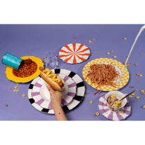 Colorful table setting with plates of food and a hand holding a hot dog on a purple background.