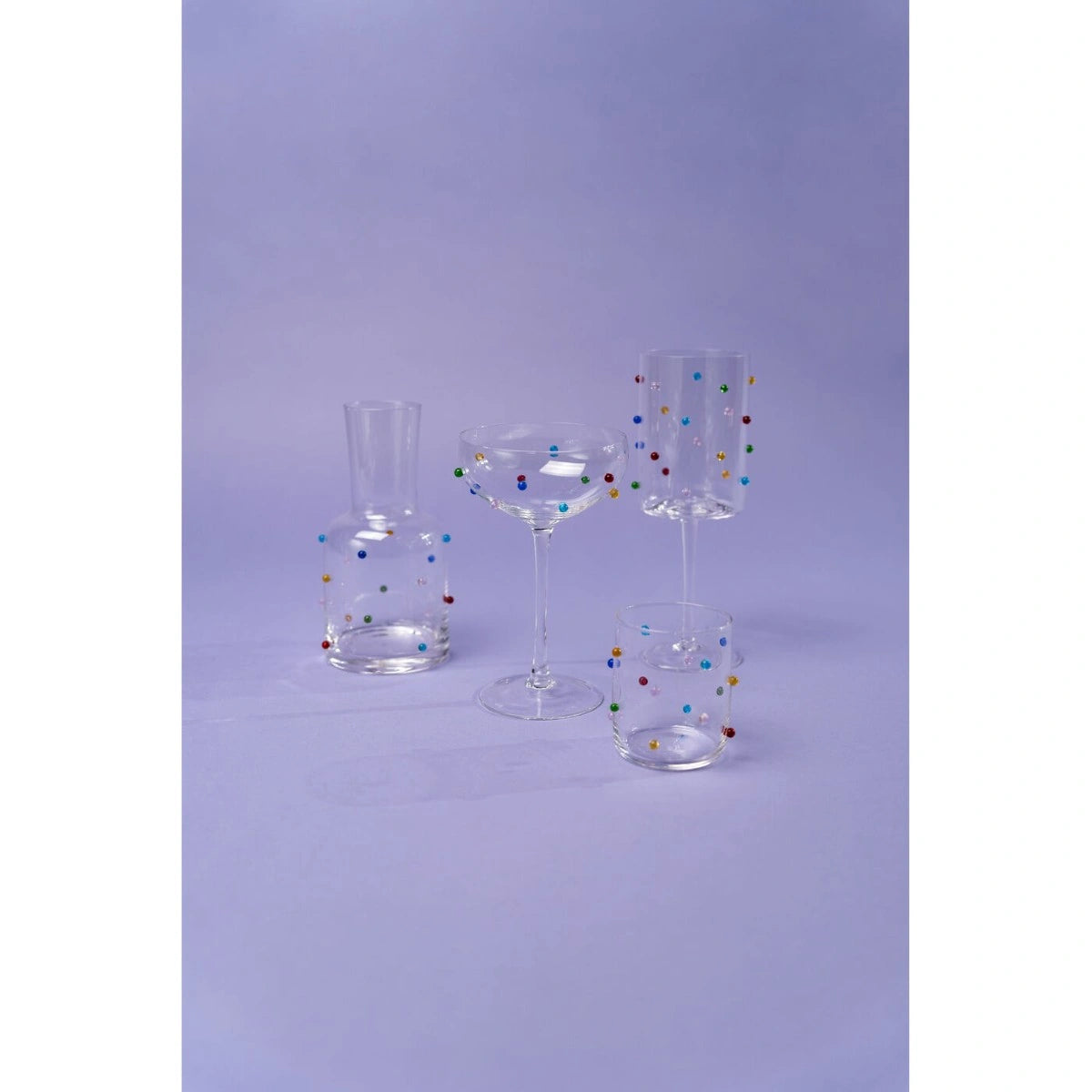 Set of four clear glass tumblers with multicolored dots on a light purple background
