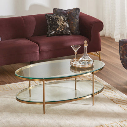 Glass coffee table with gold base in front of a maroon sofa with decorative pillows.