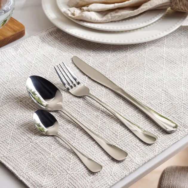 Set of silver cutlery on a textured placemat with a plate in the background- Evren 24-Piece Cutlery Set – Chrome Finish