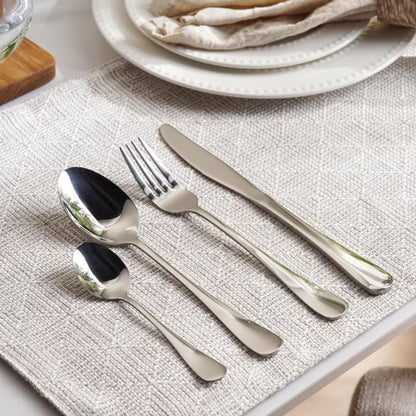 Set of silver cutlery on a textured placemat with a plate in the background- Evren 24-Piece Cutlery Set – Chrome Finish