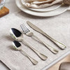 Set of silver cutlery on a textured placemat with a plate in the background- Evren 24-Piece Cutlery Set – Chrome Finish