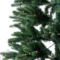 Close-up of a green artificial Christmas tree with lights on a white background