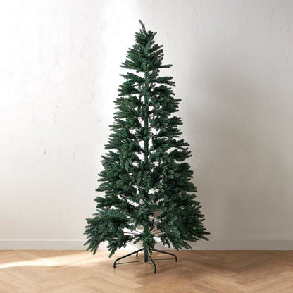 Tall artificial Christmas tree on a wooden floor with a plain white wall background