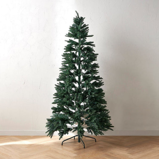 Tall artificial Christmas tree on a wooden floor with a plain white wall background