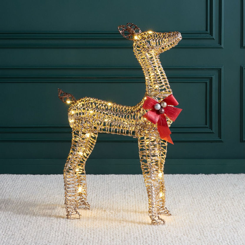 Decorative wire reindeer with lights and a red bow against a dark green wall.