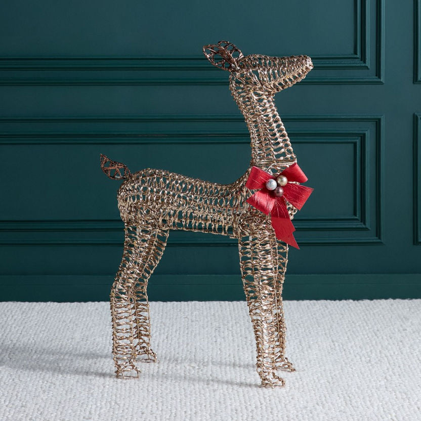 Decorative wire deer figure with a red bow and pearl on a white surface against a dark green wall.