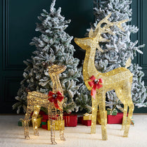 Gold deer figurines with red bows in front of a decorated Christmas tree.