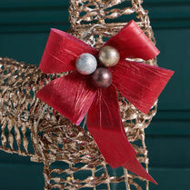 Decorative bow with red ribbon and silver and gold balls on a textured surface.