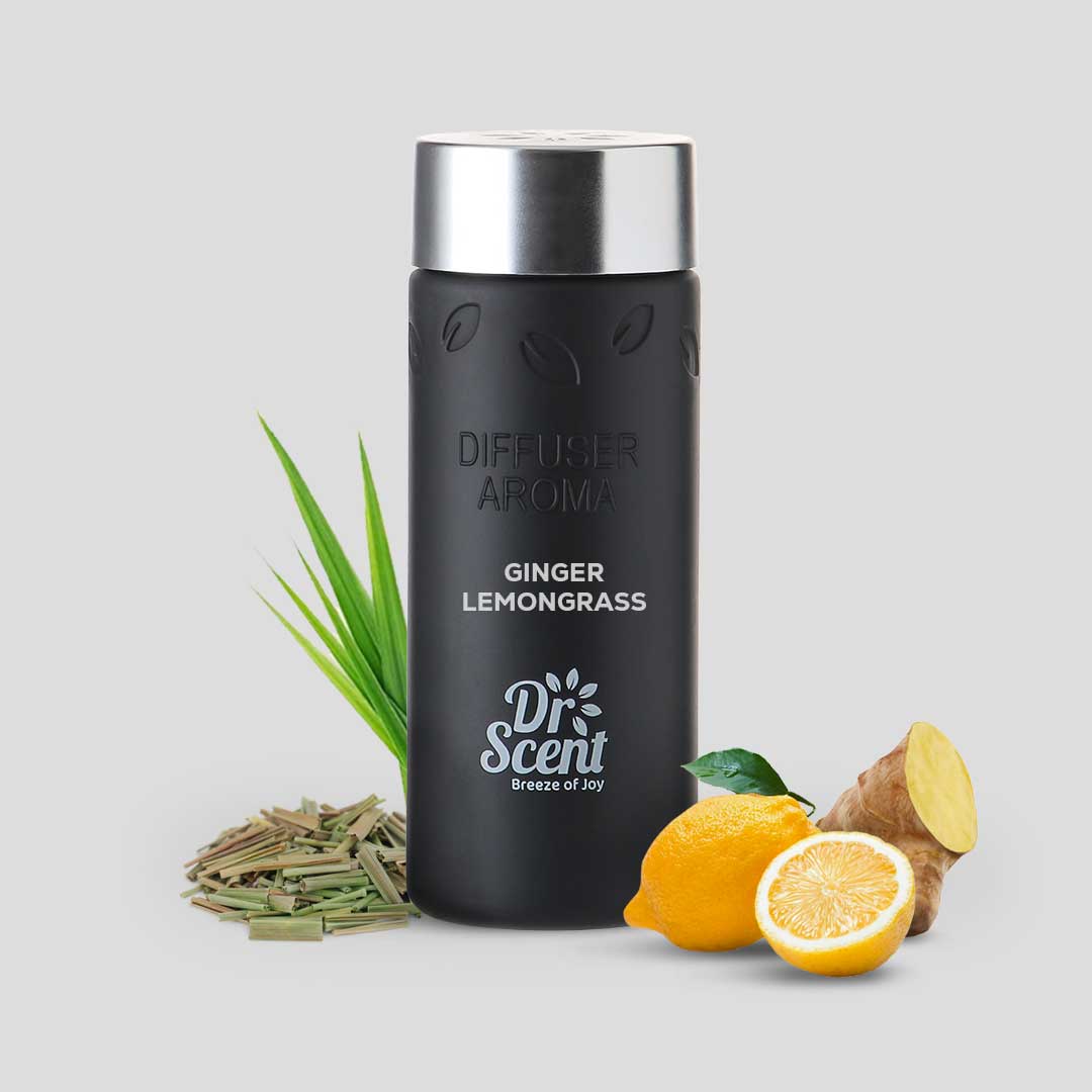 Black diffuser aroma bottle with silver cap, surrounded by ginger, lemongrass, lemon, and grass on a light gray background.