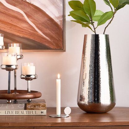 Decorative setup with a metallic vase, candles, and books on a wooden surface.