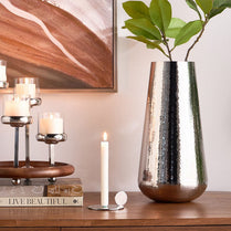 Decorative setup with a metallic vase, candles, and books on a wooden surface.