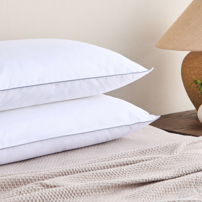 Stack of white pillows on a textured surface with a lamp and plant in the background.