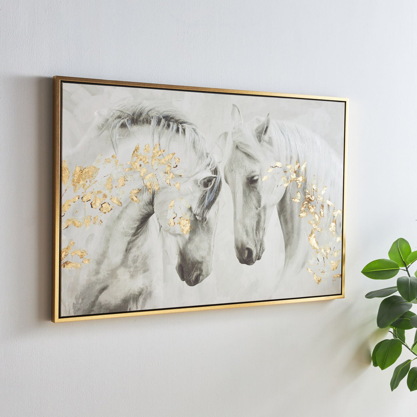 Framed artwork of two horses with gold accents on a white wall.