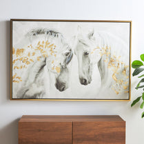 Framed artwork of two horses with gold accents on a wall above a wooden cabinet.
