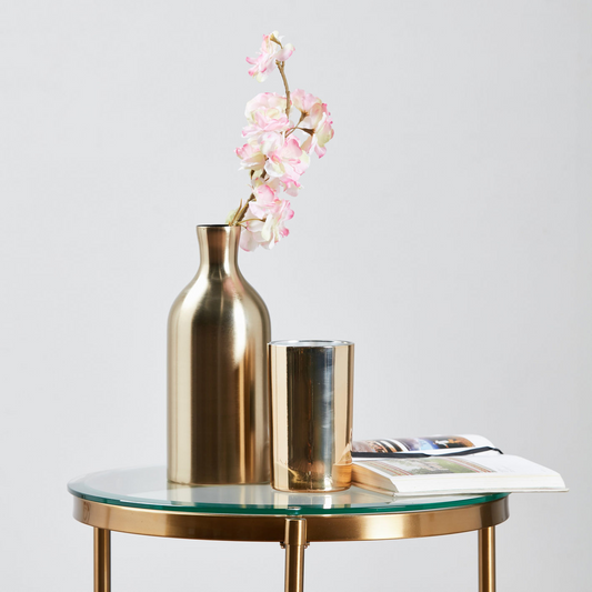 Gold vase and candle on a glass table with a white background