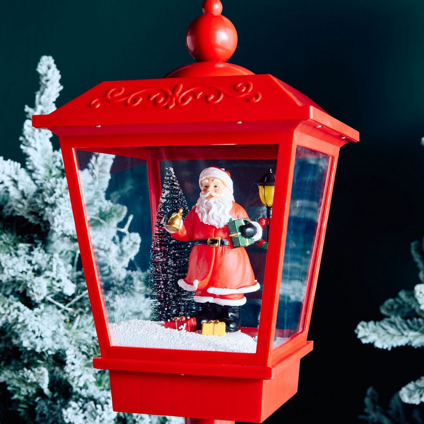 Red lantern with a Santa Claus figure inside, surrounded by snow-covered trees.