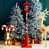 Christmas decorations including a red lamp post, candy canes, and a gold deer with a bow in front of snow-covered trees.