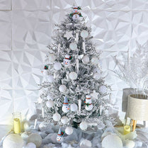 Decorated Christmas tree with snowmen and white ornaments against a geometric-patterned wall.