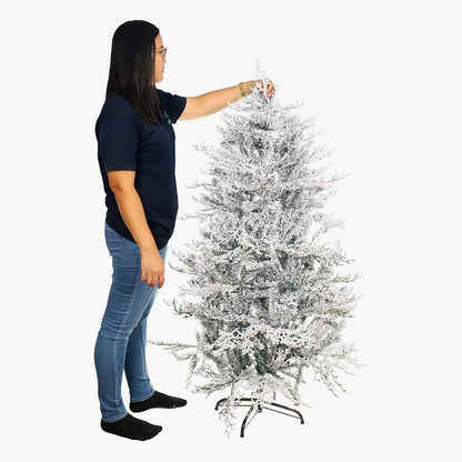 Person standing next to a flocked Christmas tree on a white background