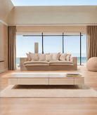 Beige sofa in a modern living room with large windows overlooking the ocean. London Collection Sofa – Minimalist Comfort for Modern Living | Vella Concept