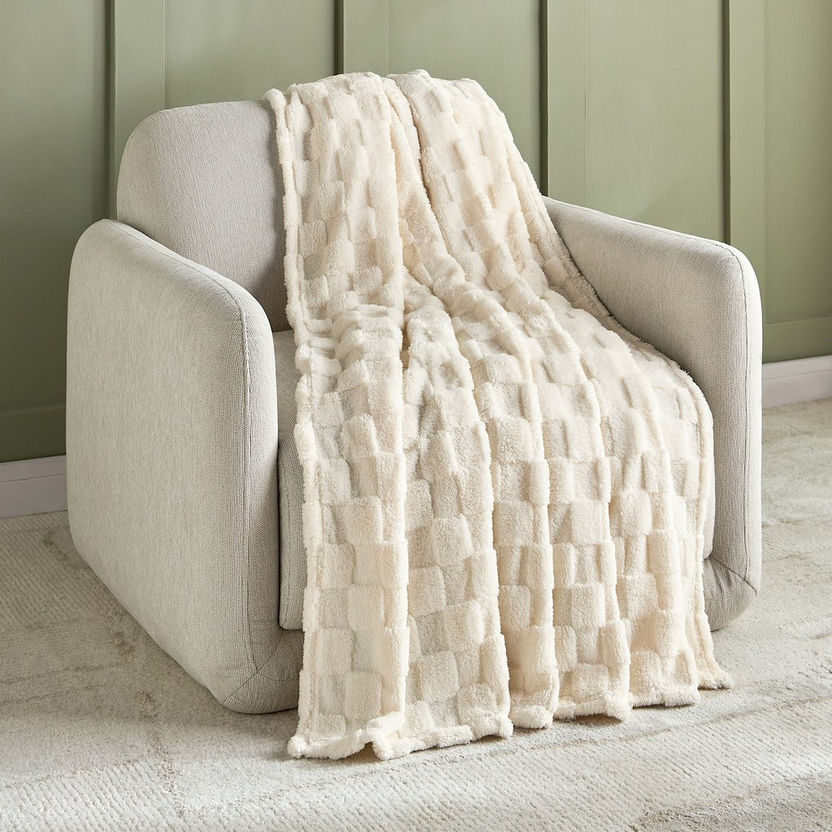 Beige textured throw blanket draped over a beige armchair against a green wall.