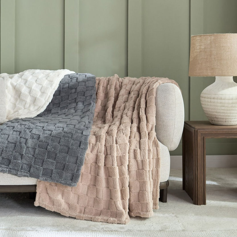 Three textured throw blankets in gray, beige, and white draped over a chair against a green paneled wall.