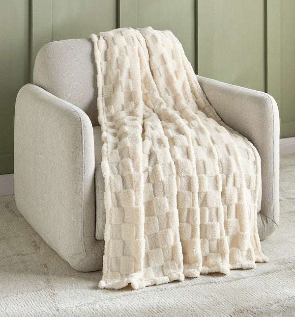 Beige textured throw blanket draped over a beige armchair against a green paneled wall.