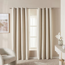 Beige curtains hanging in a room with a chair and table.