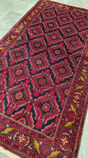 Close-up of a patterned rug with red and black colors on a light gray floor.