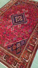 Close-up of a red patterned rug with intricate designs on a green surface- Luxury Rug Handmade Persian Rug | Handmade in Iran – Josheghan | Luxury Living Room Décor