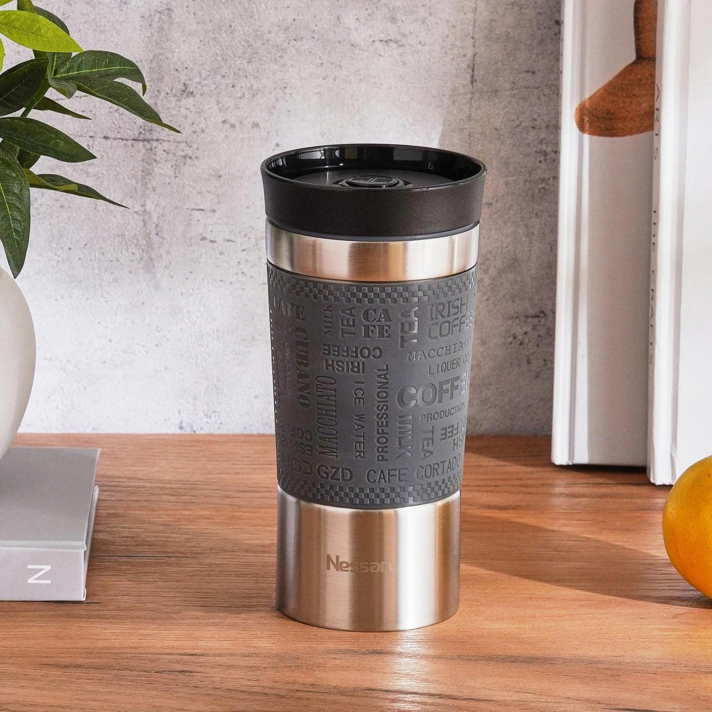 Stainless steel travel mug with black lid and textured sleeve on a wooden surface.