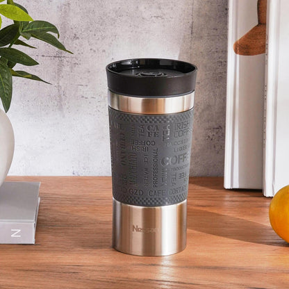 Stainless steel travel mug with black lid and textured sleeve on a wooden surface.