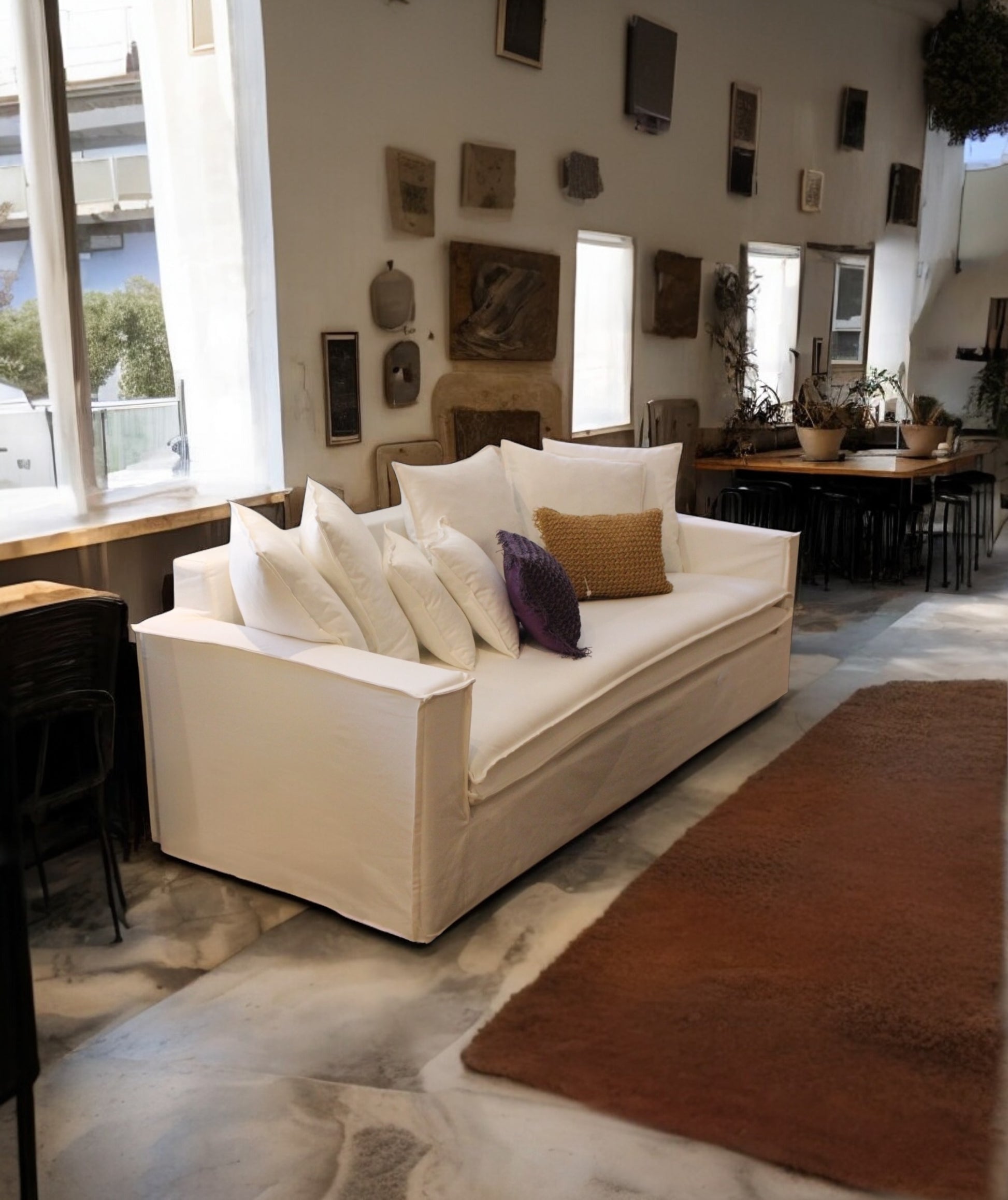 Living room with a white sofa, decorative pillows, and a dining area in the background. New York Collection Sofa – Live in the Now | Vella Concept