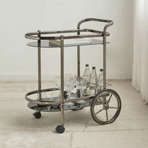 Bar cart with glass shelves and wheels in a minimalistic room.- Notica Serving Trolley - Metal & Glass 81cm