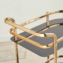 Gold-framed bar cart with a dark glass shelf on a light background- Notica Serving Trolleys- Metal & Glass, 81cm