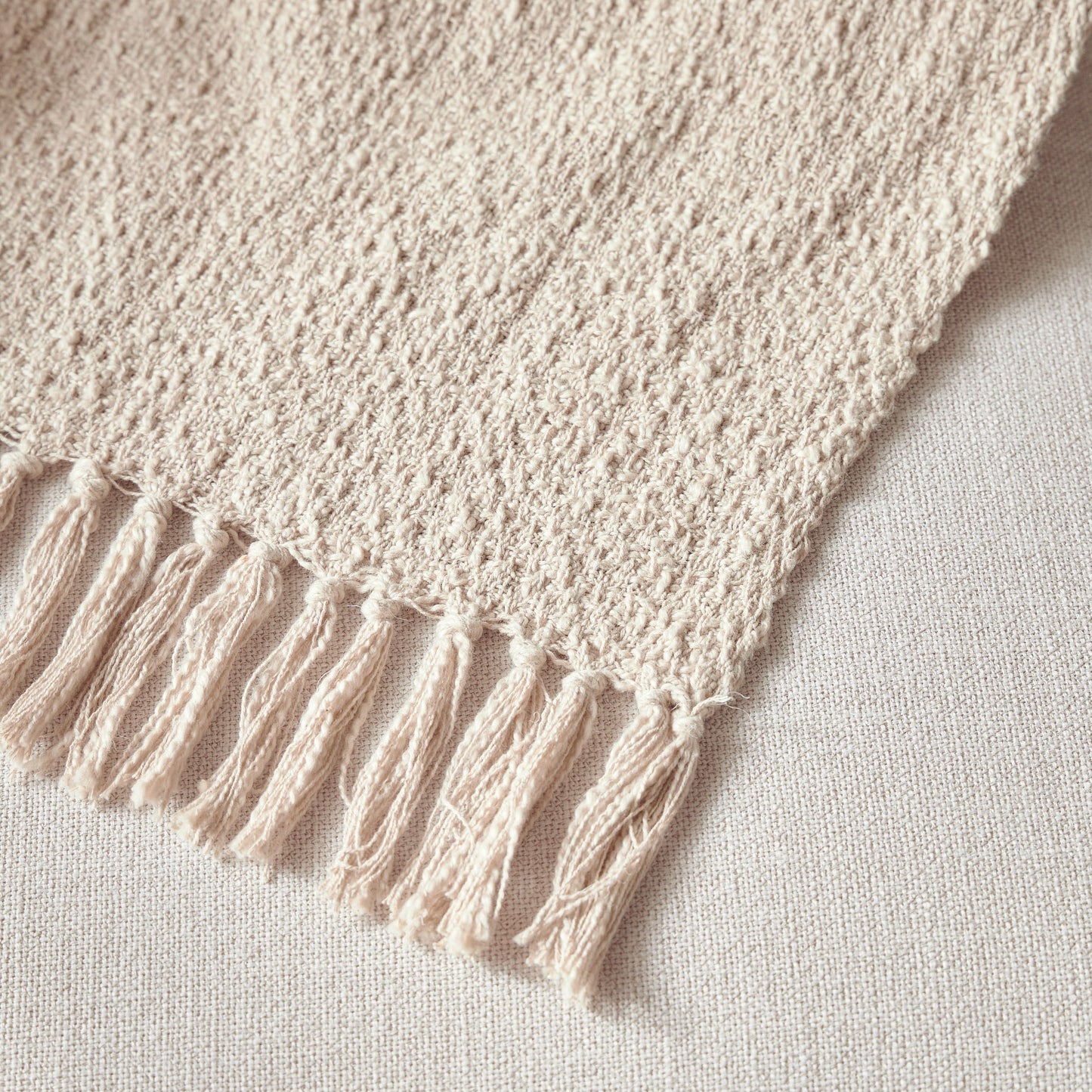 Close-up of a beige knitted blanket with tassels on a light background