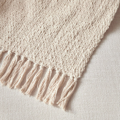 Close-up of a beige knitted blanket with tassels on a light background
