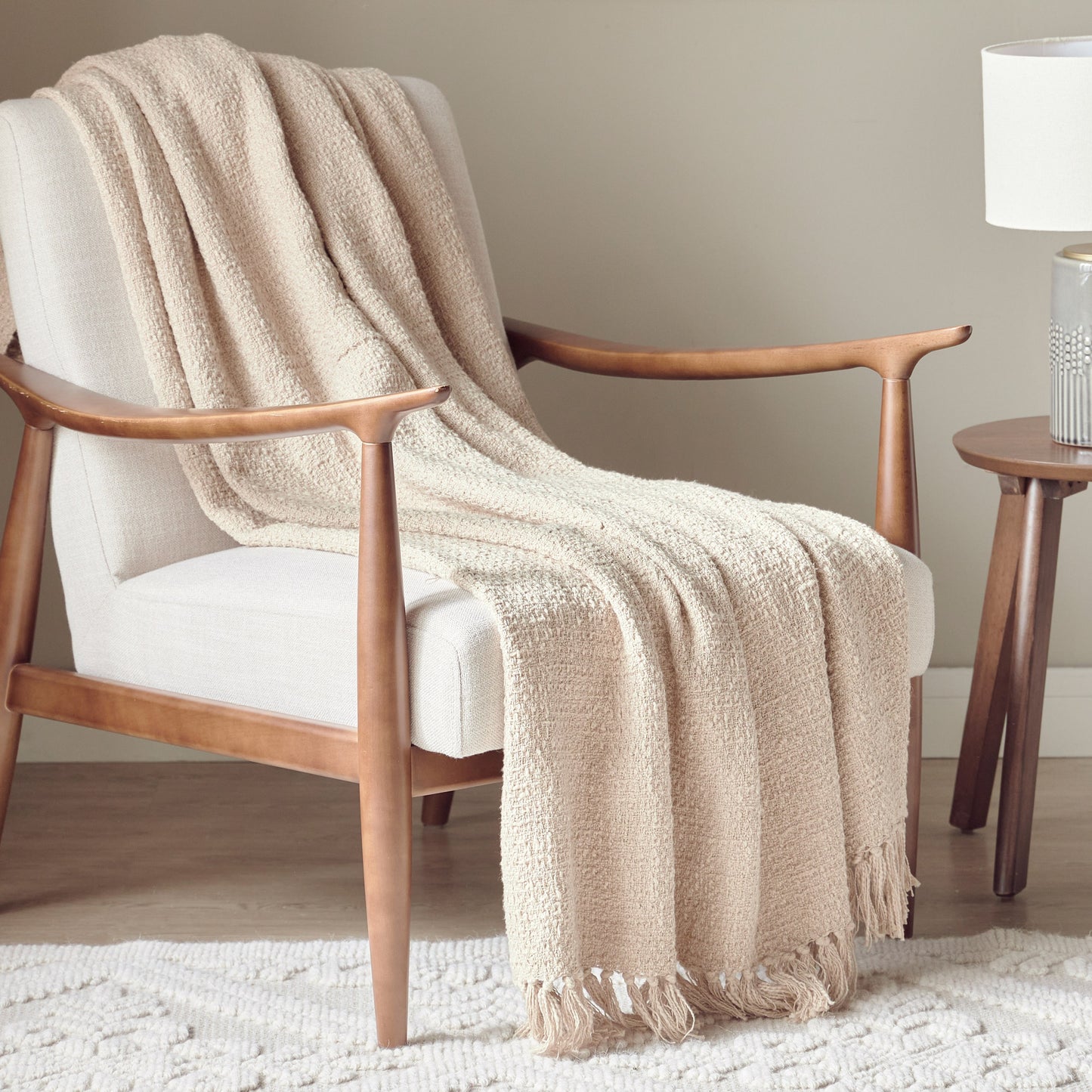 Beige blanket draped over a wooden armchair in a room with a lamp and side table.