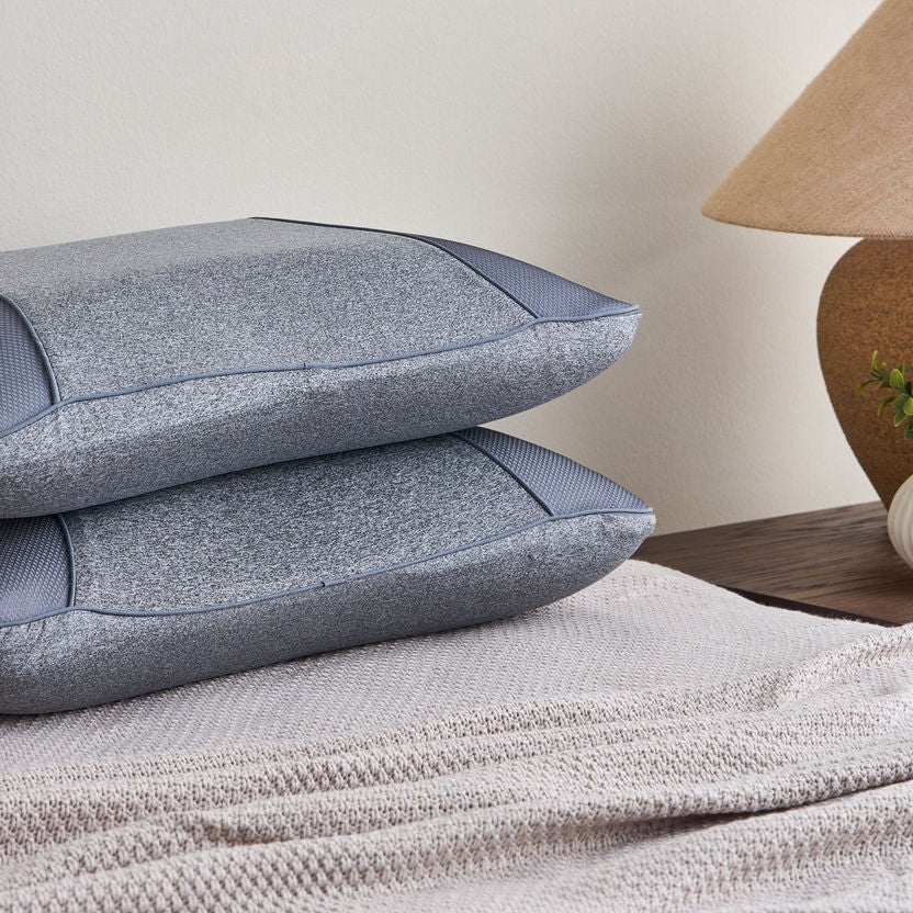 Two blue textured pillows stacked on a textured surface with a lamp in the background.