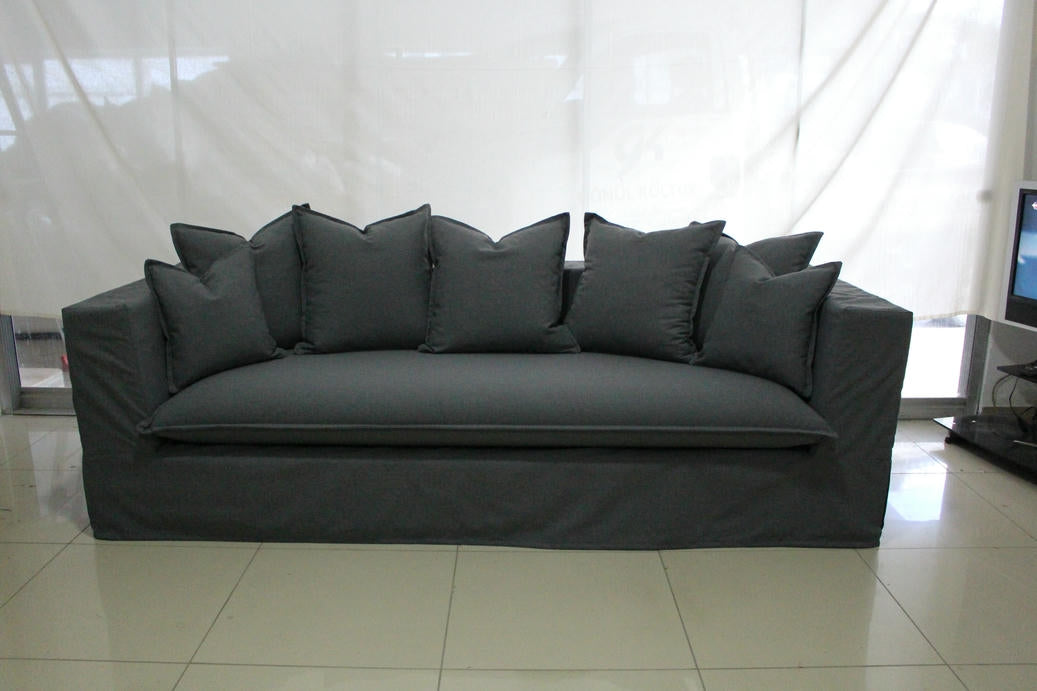 Paris Collection Sofa – Timeless Elegance | Vella Concept Gray sofa with multiple cushions in a room with white curtains and tiled floor.