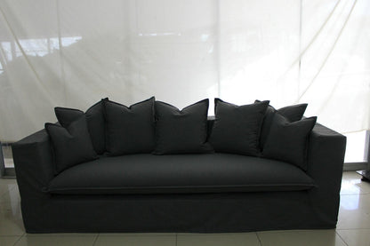 Black sofa with multiple cushions against a white curtain background. Paris Collection Sofa – Classic Elegance Reimagined | Vella Concept