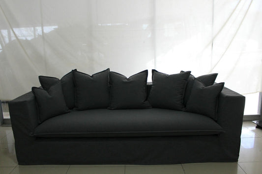 Black sofa with multiple cushions against a white curtain background. Paris Collection Sofa – Classic Elegance Reimagined | Vella Concept