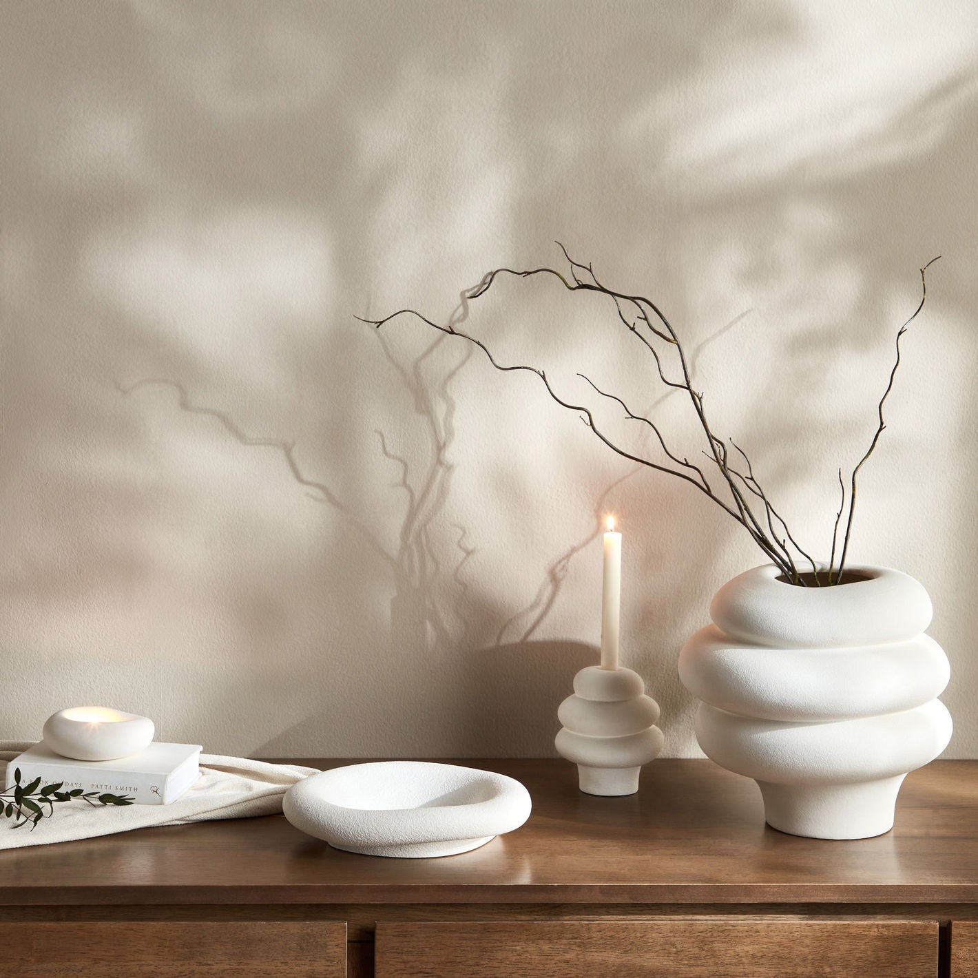 White ceramic vase with branches on a wooden surface against a neutral wall.