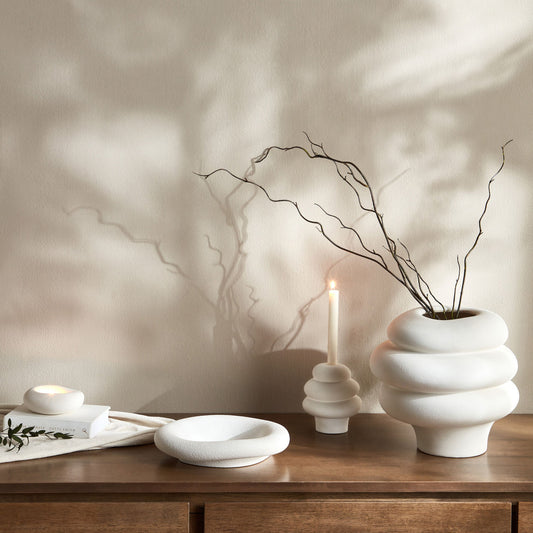 White ceramic vase with branches on a wooden surface against a neutral wall.
