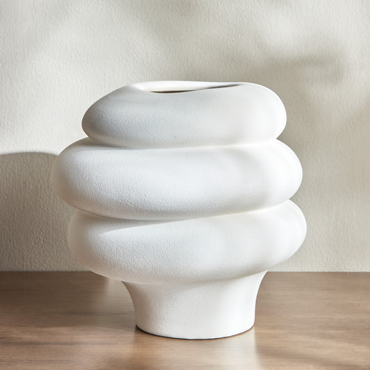 White textured vase on a wooden surface with a plain background