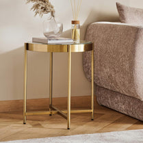 Gold side table with decorative items next to a brown sofa in a living room setting.