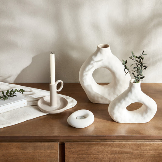 Set of white ceramic vases and candle holders on a wooden surface with a neutral background